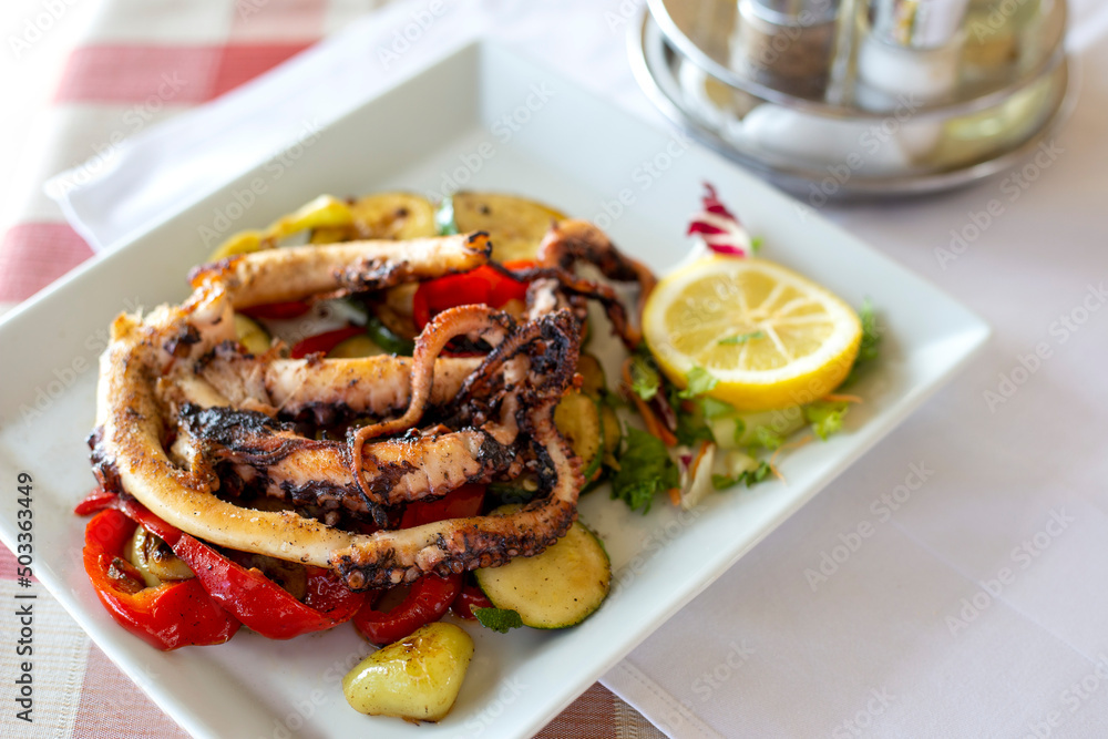 Grilled octopus with lemon and grilled zucchini in white plate on the table Grilled octopus with lemon and grilled zucchini in white plate on the table