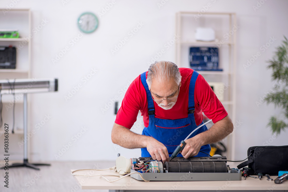 Old repairman repairing air-conditioner at workshop Old repairman repairing air-conditioner at workshop