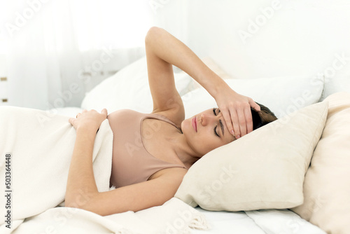 Depressed sad young woman lying in bed suffering from headache. Upset stressed millennial woman relaxing in home bedroom, feeling sick, suffering from illness or depression