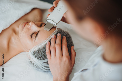 Top view of a woman receiving ultrasound cavitation facial peeling in spa salon. Happy face. Cosmetology beauty procedure. Facial skincare. photo