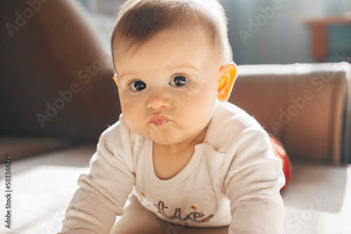 Caucasian baby lying on stomach with serious face looking at camera. Family care. Baby care.