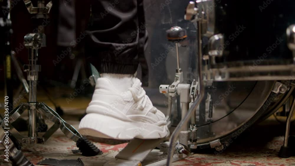 Closeup shot of drummers foot of playing drums using pedal for hitting drum. Drummers foot in white sneakers moving drum bass pedal. Back view. Music, drums concept Closeup shot of drummers foot of playing drums using pedal for hitting drum. Drummers foot in white sneakers moving drum bass pedal. Back view. Music, drums concept