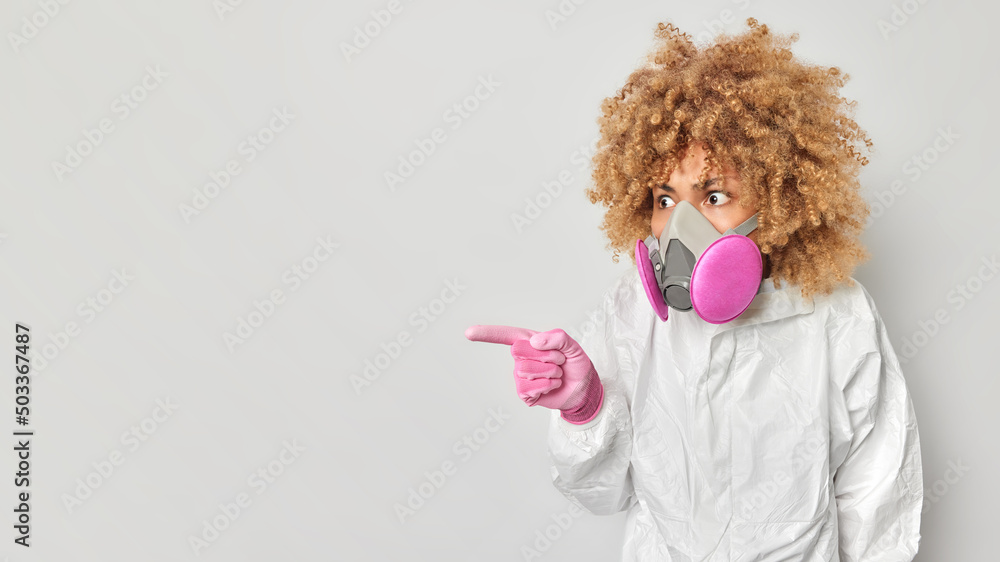 Impressed woman dressed in protective clothes wears respirator points