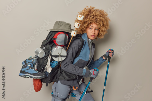 Canvas Print Serious curly haired female hiker focused into distance carries rucksack with ne