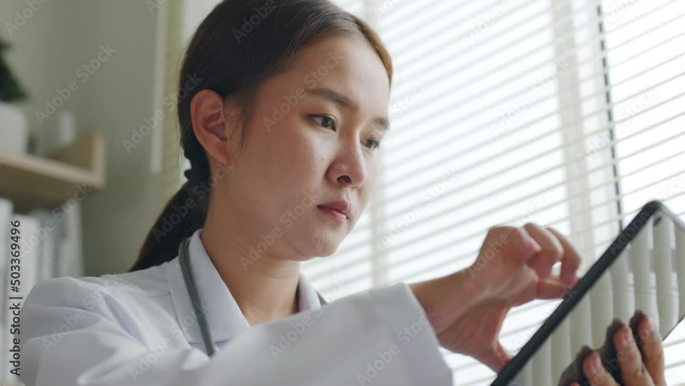 Asian woman doctor reading medical report on tablet, working in medical office hospital Asian woman doctor reading medical report on tablet, working in medical office hospital