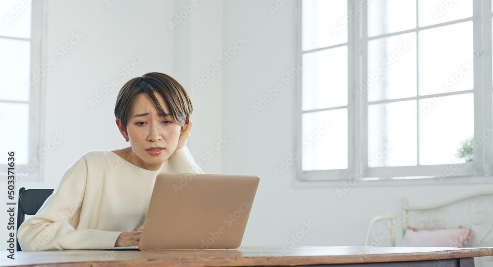 ノートパソコンを見ながら悩む女性