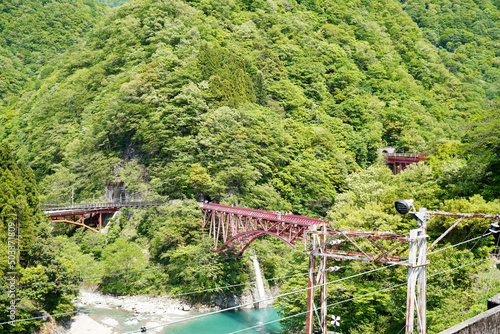 赤い鉄橋の背景に広がる美しいい自然の山々の美しい風景写真・黒部峡谷鉄道・黒部峡谷・富山県観光地
