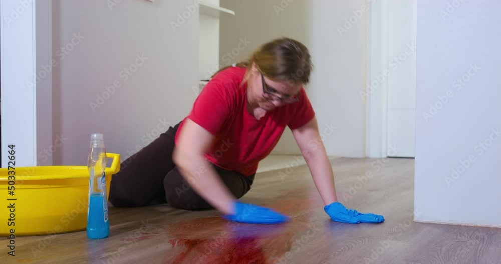 Young plump woman washes blood stain from wooden parquet. Blonde lady in rubber gloves uses cloth and detergent cleaning floor from dirt and blood Young plump woman washes blood stain from wooden parquet. Blonde lady in rubber gloves uses cloth and detergent cleaning floor from dirt and blood
