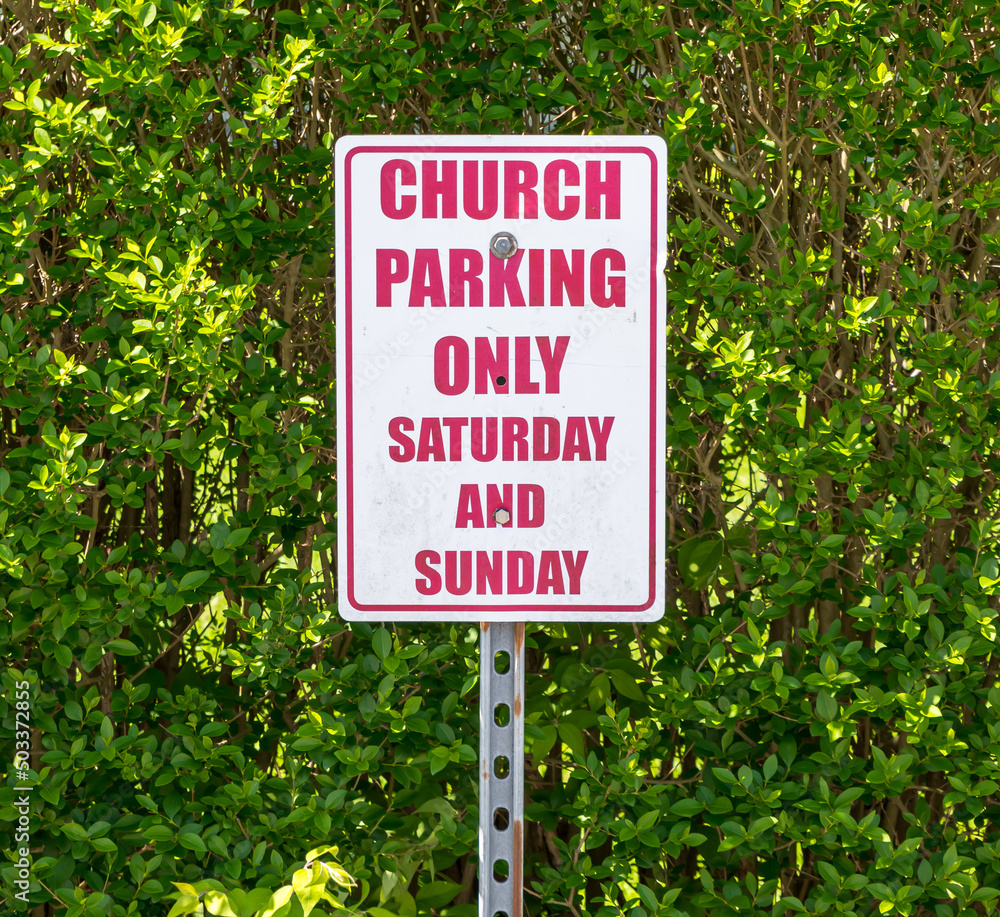 A church parking sign in front of green hedges on a sunny spring day