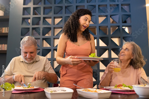 Família brasileira jantando. Mãe conversando feliz com avós