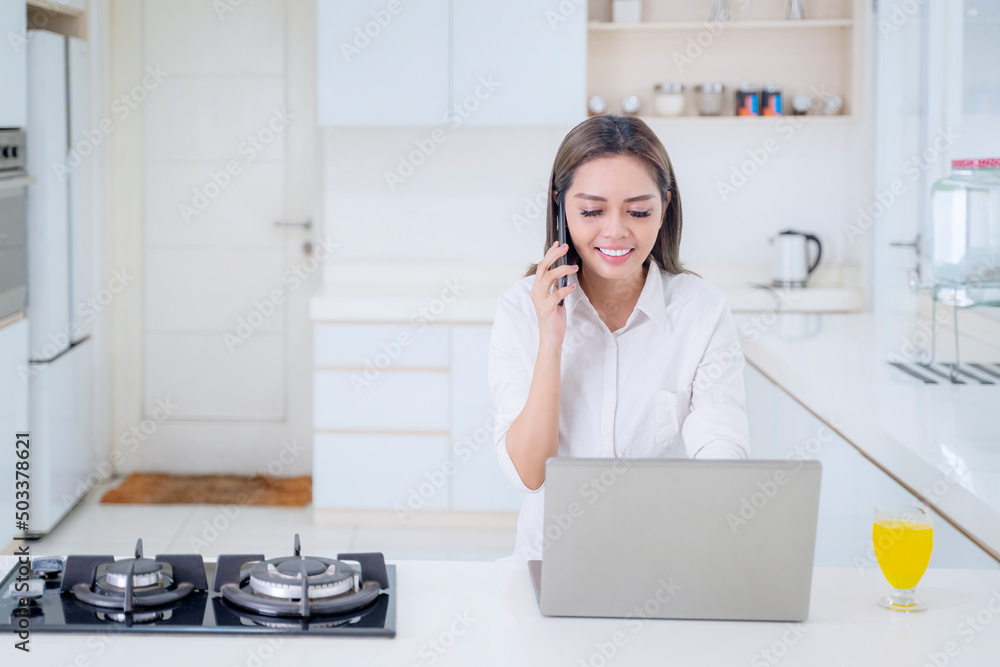 Happy woman using cellphone and laptop in kitchen Happy woman using cellphone and laptop in kitchen