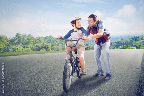 Little boy learning to ride a bicycle with father