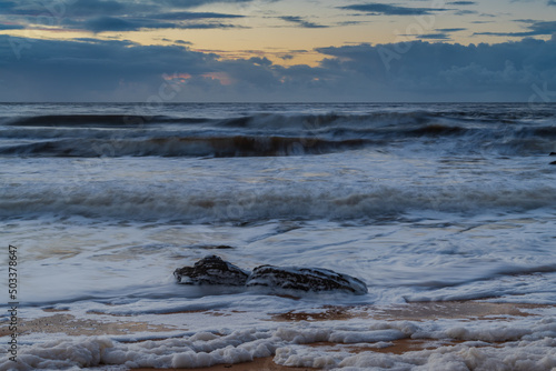Sunrise seascape with sea foam and rain clouds