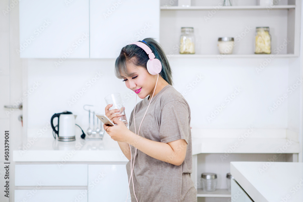Woman drinking water while enjoying music in kitchen