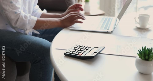 Close up of young woman hands type on laptop and digital calculator check sum of utility bills before make payment online in ebank app. Millennial female balance domestic budget prepare to pay taxes photo