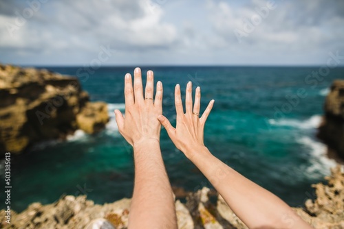 Two young just married hands with wedding rings on a tropical ocean background 