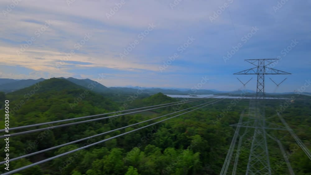 An aerial view tilts down from above over industrial utility power lines and columnar structures in green and rural patterned farmland. An aerial view tilts down from above over industrial utility power lines and columnar structures in green and rural patterned farmland.