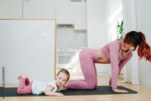 Loving mother doing yoga, standing on all fours next to her baby on a mat