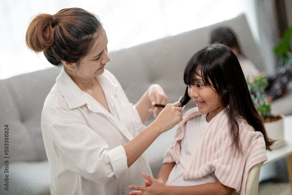 Asian Mother cutting hair to her daughter in living room at home while stay at home safe from Covid-19 Coronavirus during lockdown. Self-quarantine and social distancing concept. Asian Mother cutting hair to her daughter in living room at home while stay at home safe from Covid-19 Coronavirus during lockdown. Self-quarantine and social distancing concept.