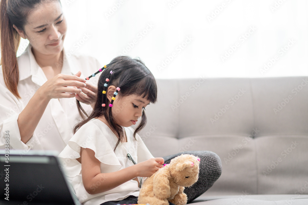 Young Asian mother tying daughter's hair Young Asian mother tying daughter's hair