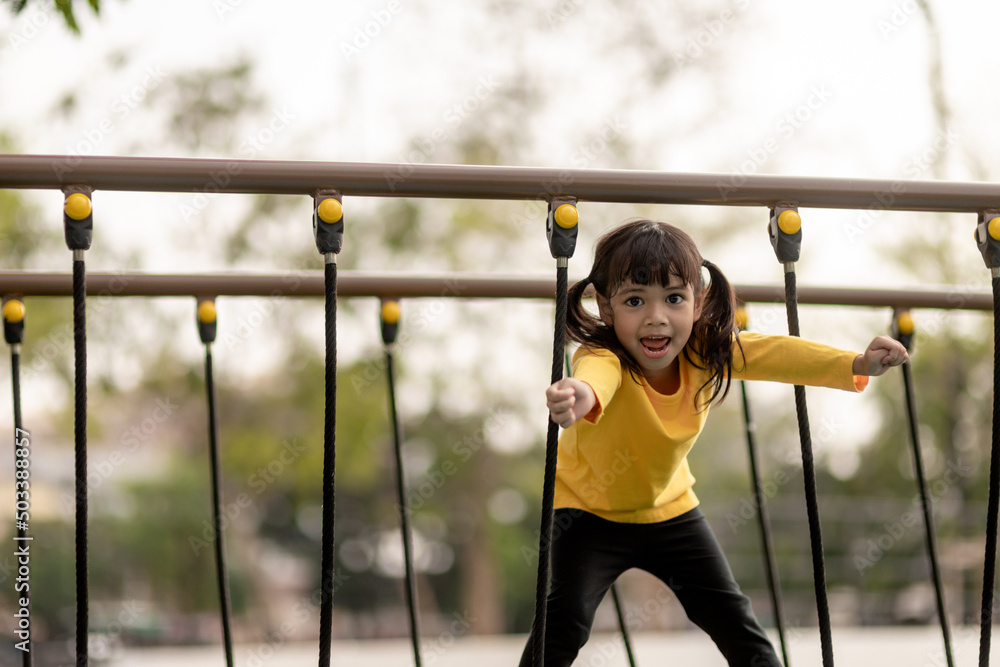 Fototapeta premium summer, childhood, leisure and people concept - happy little girl on children playground climbing frame