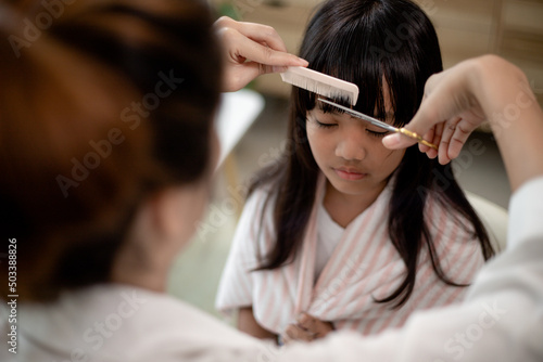 Asian Mother cutting hair to her daughter in living room at home while stay at home safe from Covid-19 Coronavirus during lockdown. Self-quarantine and social distancing concept.