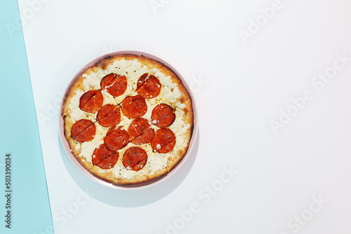 Italian pizza with pepperoni and cheese on coloured background. Cheese focaccia with salami in minimal style on blue and orange color. American pizza delivery concept with color backdrop