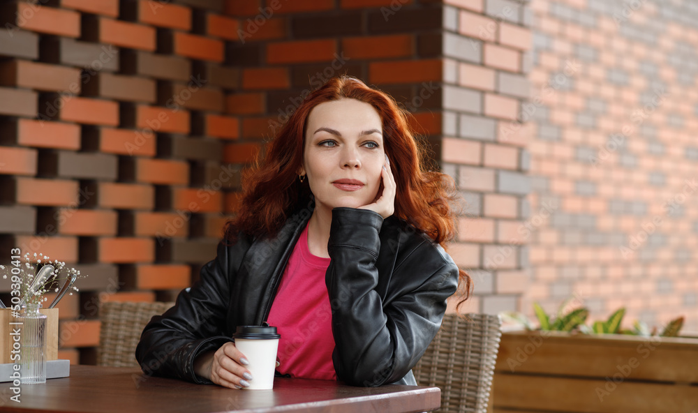 Fototapeta premium An adult woman is sitting in a summer cafe with a cup of coffee and smiling