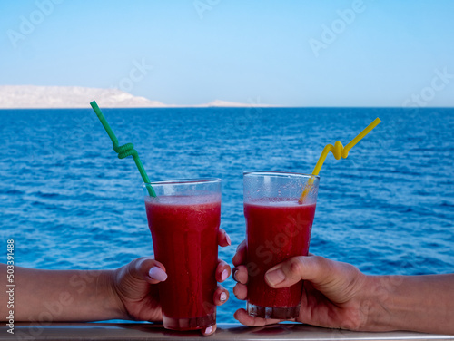 Two female hands hold glasses with fruit cocktails on the background of the sea.