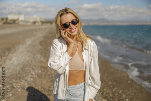 Lovely lady in sunglasses smiling while talking on the phone while standing on a beach