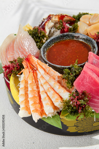 Sashimi set from raw seafood: salmon, tuna, eel, perch, shrimps, sea scallop. Traditional japanesse dish - sashimi on white background. Fresh delicacy on ice with lemon, ginger and sauce.