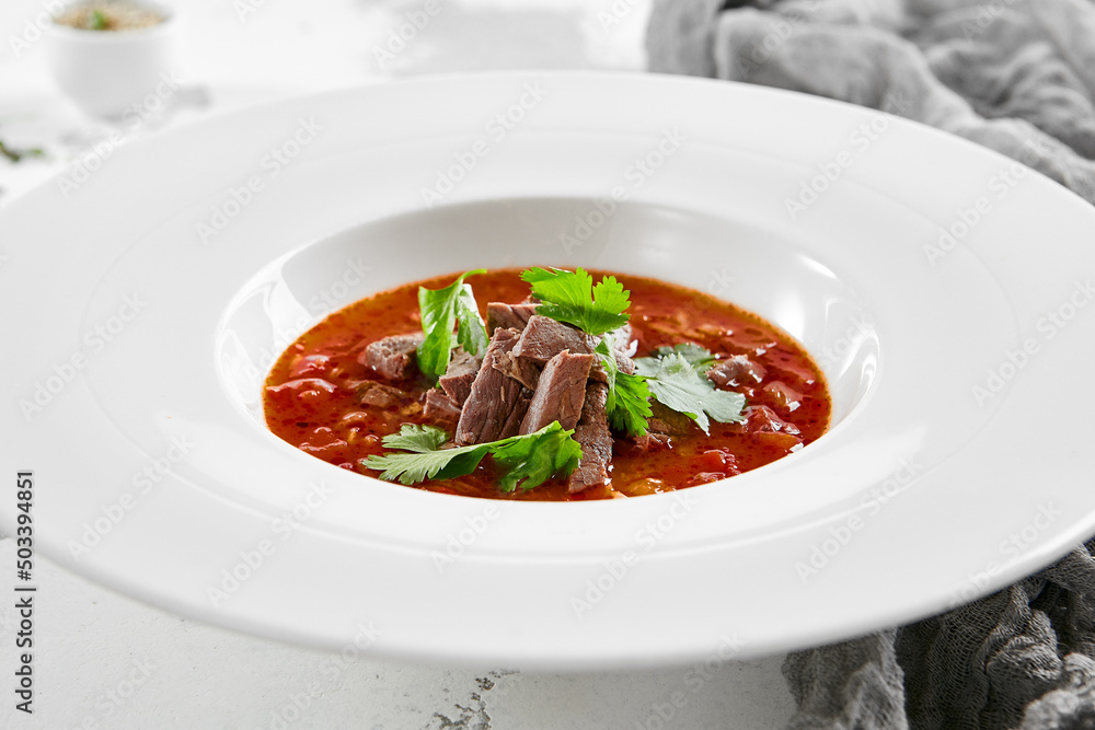 Authentic georgian beef soup Kharcho. Georgian lamb and rice soup. Caucasian dish - kharcho soup with rice, beef and coriander leaves. Kharcho in white plate on stone table. Authentic georgian beef soup Kharcho. Georgian lamb and rice soup. Caucasian dish - kharcho soup with rice, beef and coriander leaves. Kharcho in white plate on stone table.