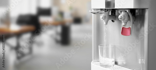 Bild auf Leinwand Pouring of fresh water from modern cooler into glass in office, closeup