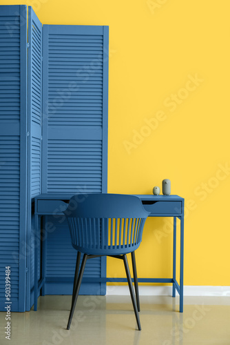 Blue folding screen, table and chair near yellow wall