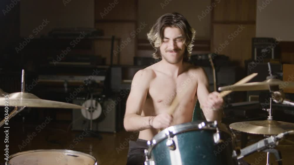 Young shirtless male drummer with beard playing drums at music studio while rehearsing alone. Musician performing on percussion instruments. Music, leisure concept