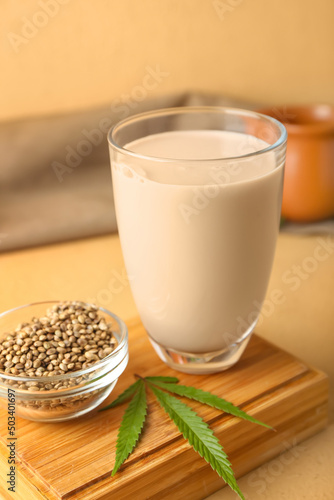 Glass of hemp milk and bowl with seeds on color background, closeup photo