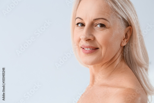 Mature blonde woman with healthy skin smiling on light background  closeup