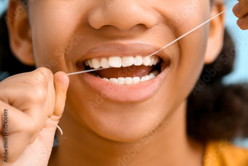 African-American teenage girl flossing teeth on blue background, closeup