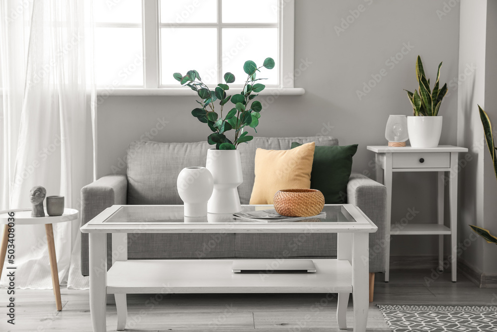 Interior of light living room with sofa, houseplants and vases with eucalyptus - obrazy, fototapety, plakaty 
