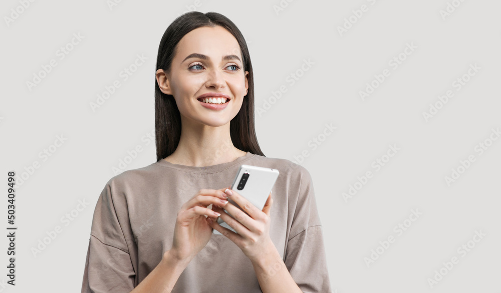 Beautiful young woman with mobile phone isolated studio portrait, Smiling student girl holding smartphone over gray background Beautiful young woman with mobile phone isolated studio portrait, Smiling student girl holding smartphone over gray background