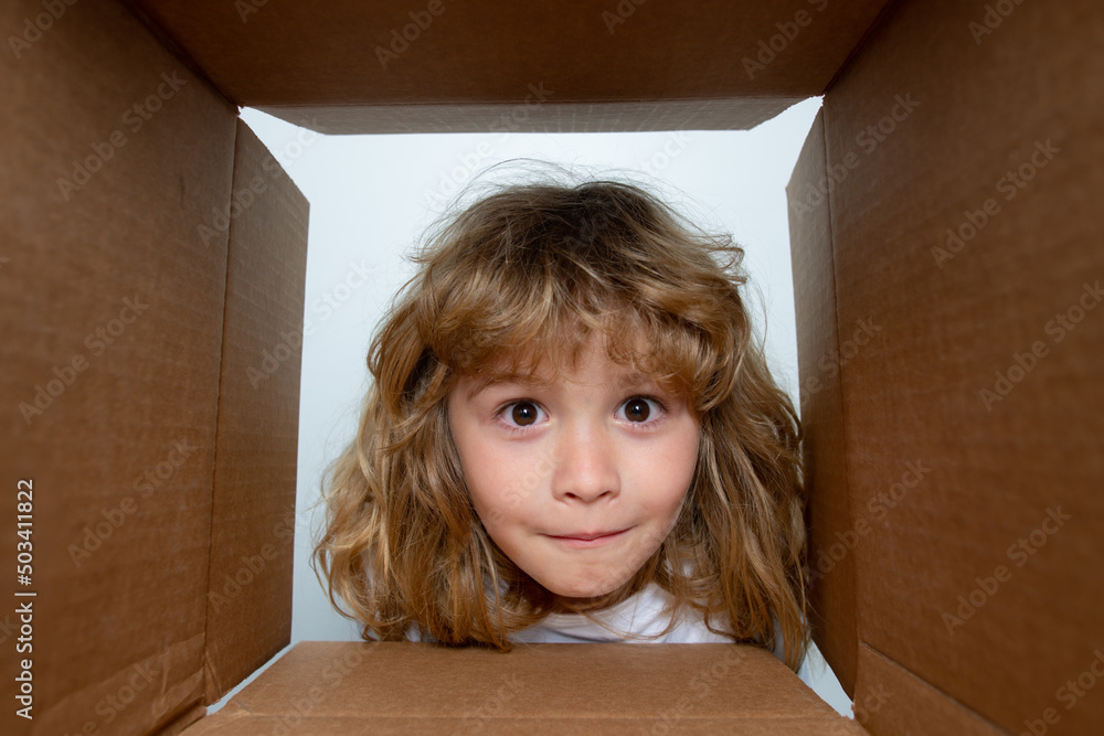 Kid boy unpacking and opening carton box looking inside with surprise face. Children expression surprised face. Kid boy unpacking and opening carton box looking inside with surprise face. Children expression surprised face.