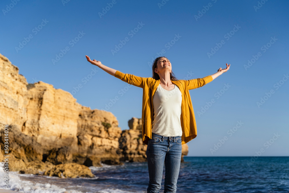 Smiling woman with arms outstretched standing at beach on sunny day Smiling woman with arms outstretched standing at beach on sunny day