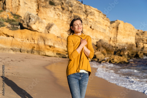Smiling woman wearing shrug standing in front of rock formation on shore at beach