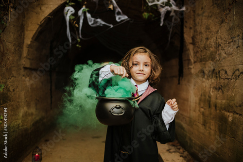 Cute girl holding cauldron with witches brew wearing witch costume in spooky tunnel