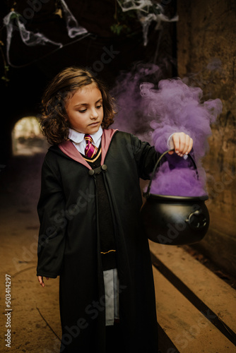 Cute girl holding cauldron with witches brew wearing witch costume in spooky tunnel photo