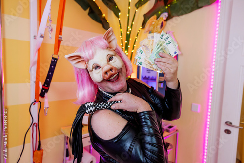 Happy transvestite man wearing pig mask holding whip and paper currency photo