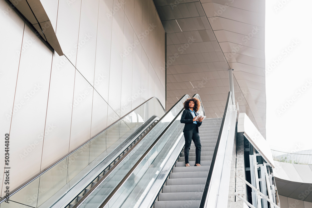 Businesswoman holding tablet PC standing on escalator Businesswoman holding tablet PC standing on escalator