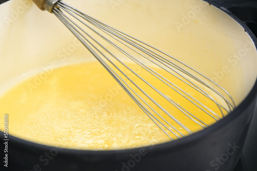 Wire whisk in a pot with golden yellow semolina flummery or pudding, cooking a delicious dessert, copy space, selected focus photo