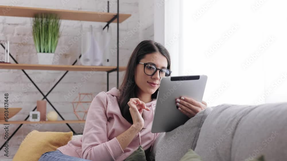 Attractive brunette Girl in glasses using digital tablet at home. Portrait of young beautiful female texting on digital tablet in living room. Joyful smiling woman using gadget. Technology concept. Attractive brunette Girl in glasses using digital tablet at home. Portrait of young beautiful female texting on digital tablet in living room. Joyful smiling woman using gadget. Technology concept.