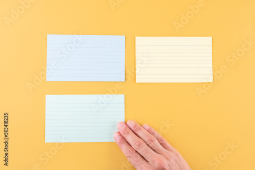 hand putting blank writing paper and two empty papers on a yellow background. space for text.